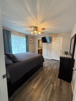 Une chambre à coucher avec un lit, un ventilateur de plafond, une télévision et une porte.