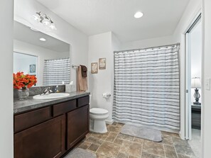 Une salle de bain avec un lavabo en marbre, des meubles en bois foncé, des toilettes et un rideau de douche à rayures.