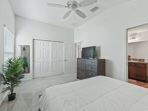 Une chambre à coucher comprenant un lit, une commode, un téléviseur, un ventilateur de plafond et une porte.