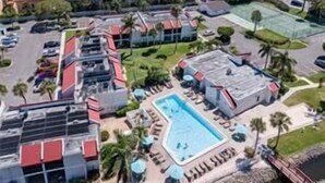 Ett flygbildsbild av ett semesterområde med flera byggnader, en swimmingpool och palmer.