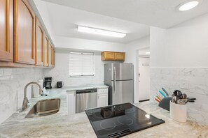 A modern kitchen with a built-in dishwasher, stainless steel refrigerator, and a black induction cooktop. - Spend a month away, just a quick walk to the sand! (Bradenton Beach)