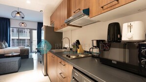 A modern kitchen with wooden cabinets, a stainless steel sink, a coffee maker, and a microwave. - Premium Studio in Oasis - 318 (Abu Dhabi)