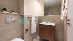 A modern bathroom with a toilet, sink, and shower. There are two potted plants on the wall, a towel hanging on a rack, and a mirror above the sink. - Premium Studio in Oasis - 318 (Abu Dhabi)