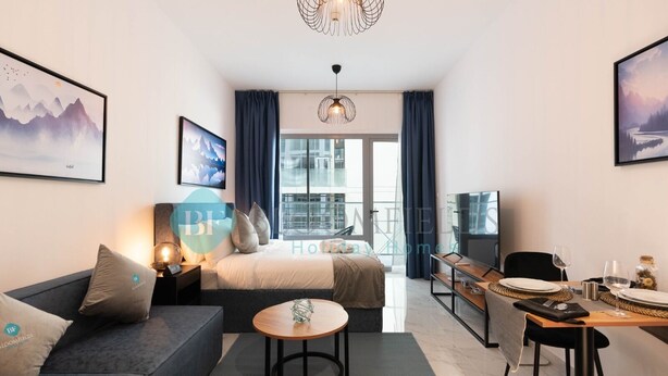 A modern hotel room with a bed, sofa, dining table, and a balcony with a city view. - Premium Studio in Oasis - 318 (Abu Dhabi)