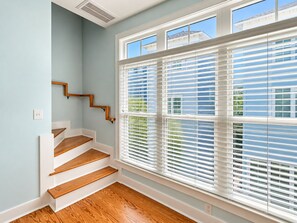 A staircase with wooden steps and white walls, leading to a room with large windows and blinds.
