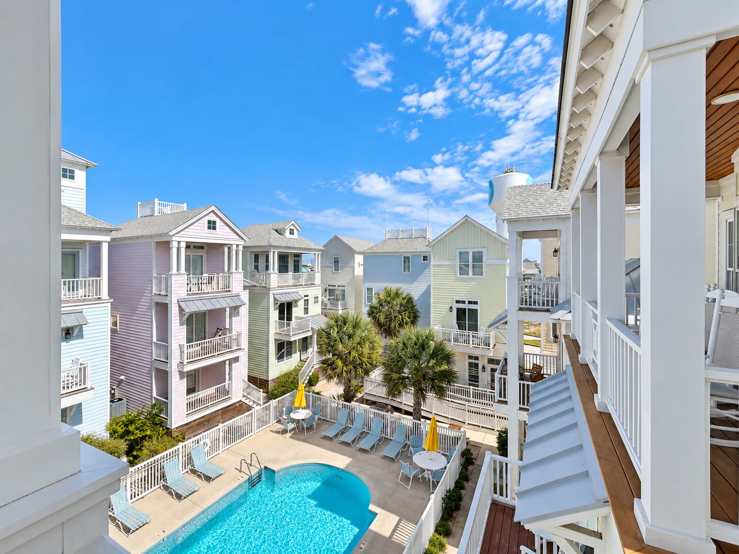A multi-story hotel with a swimming pool, balconies, and a clear blue sky.