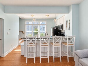 A modern kitchen with white cabinetry, a central island with bar stools, and pendant lighting.