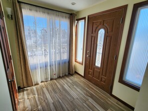 Ein Zimmer mit Holzboden, einer großen Holztür mit Glaseinsätzen und einem Fenster mit Blick auf Bäume.