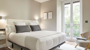 A modern bedroom with a large bed, bedside lamps, a chair, and a view of the outdoors. - Elkano by FeelFree Rentals (Donostia)