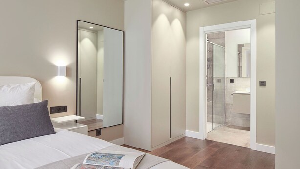 A modern bedroom with a large bed, a bedside table, a mirror, and a walk-in closet. - Elkano by FeelFree Rentals (Donostia)