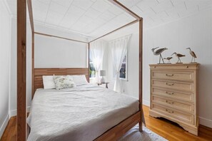 Una cama con dosel y tablero de madera, un aparador con esculturas de pájaros y una ventana con cortinas de gasa.