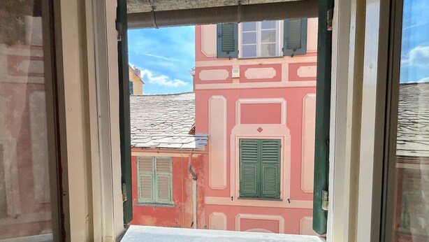 Ein Fenster mit Blick auf ein Gebäude mit roten und rosafarbenen Fassaden und grünen Fensterläden.