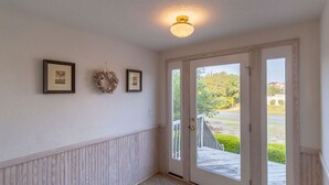 A hallway with a door leading to a deck, framed pictures on the wall, and a light fixture above. - Near the Beach! Saltwater Pool, Hot Tub, Great Neighborhood, C0949 (Corolla)