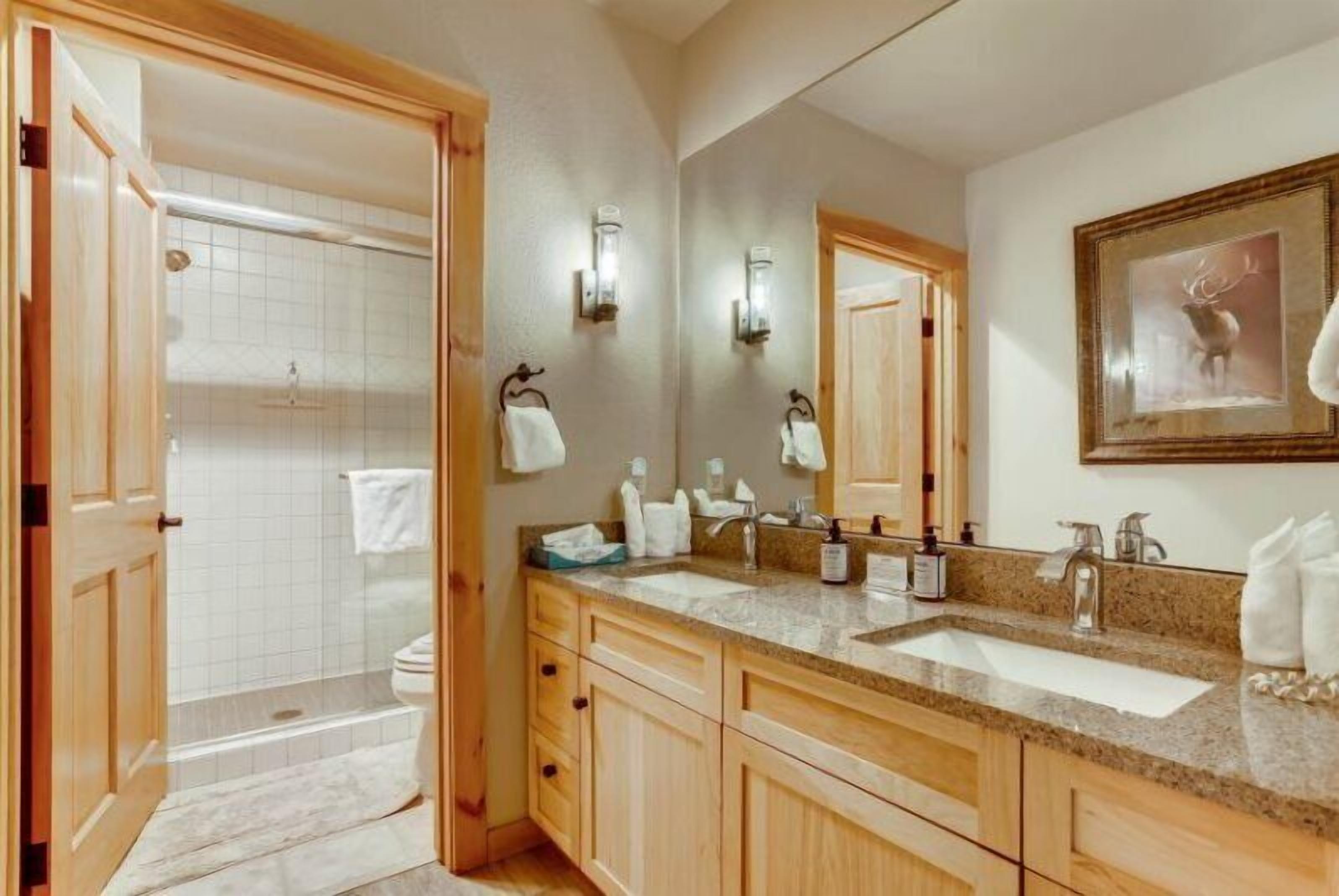 A bathroom with a double sink, wooden cabinets, a large mirror, and a framed deer picture on the wall.
