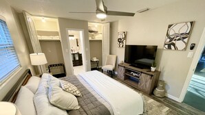 Habitación de hotel con una cama grande, televisión, escritorio y silla. Se observa un vestidor y un baño a través de una puerta abierta.