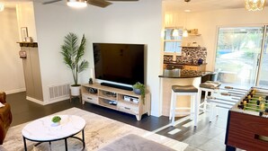 Una sala de estar moderna con un televisor de pantalla plana, un sofá, una mesa de centro y una zona de cocina con una mesa de futbolín.