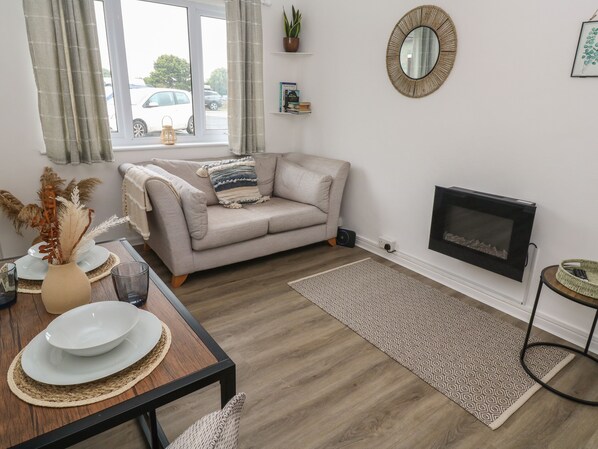 A living room with a sofa, a fireplace, a dining table with plates, a vase with dried plants, and a view of the outside through a window.