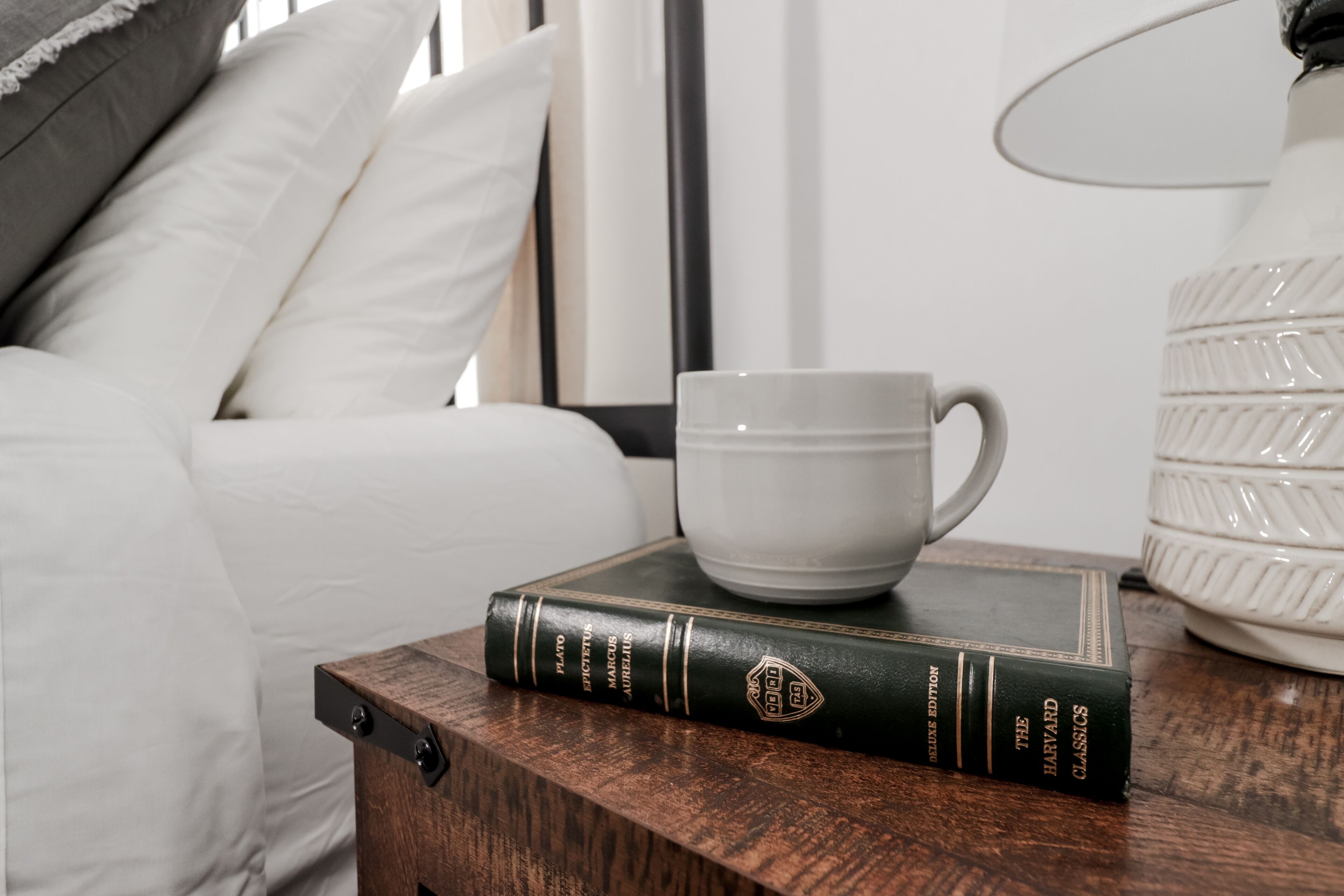 A wooden nightstand with a book titled "The Harvard Classics" and a white mug.