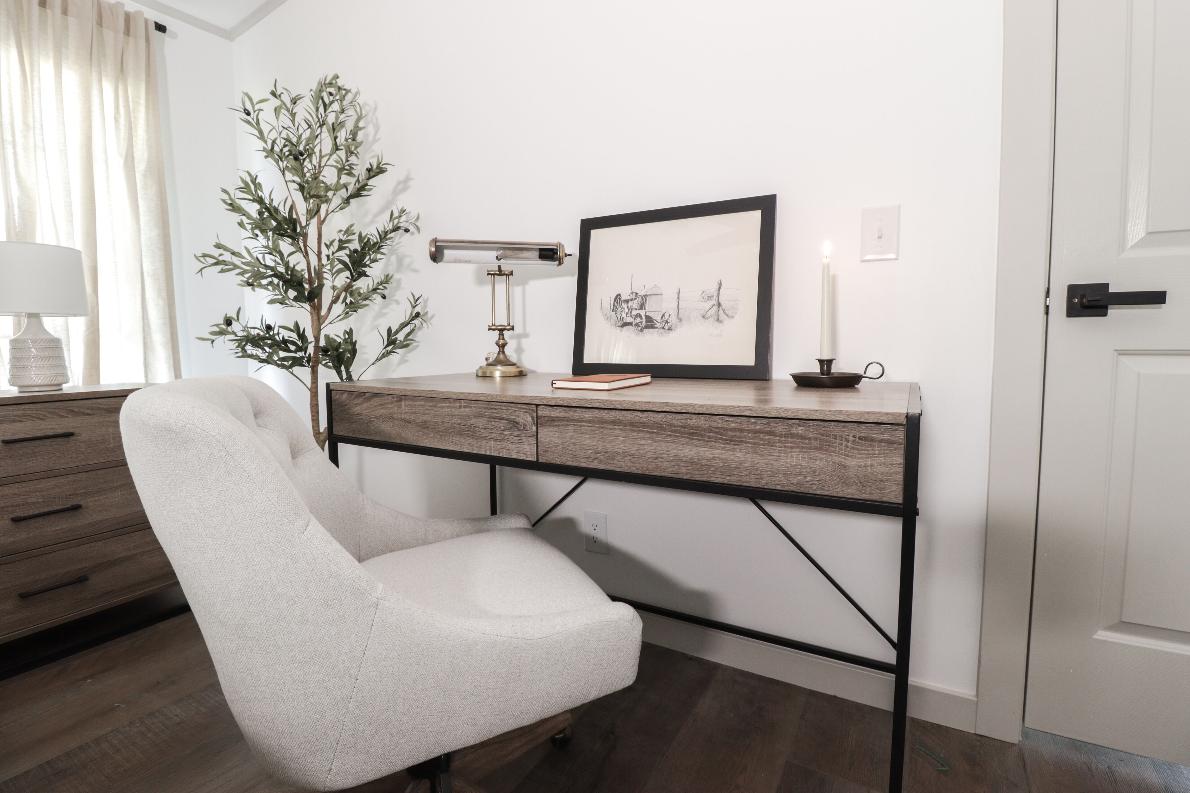 A modern desk with a white chair, a framed picture, a desk lamp, and a candle on the desk.