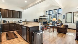 A spacious kitchen with dark wood cabinets, a large island, and a stone fireplace. - Breckenridge White Wolf Townhome 4 Bedroom (Breckenridge)