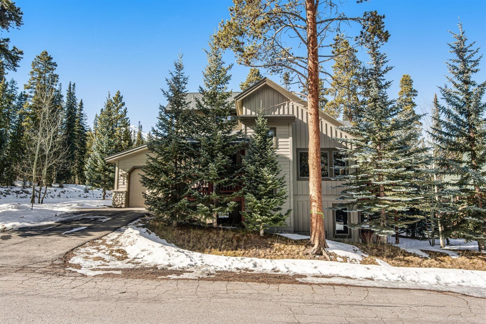 Une maison à deux étages avec un garage, entourée d’arbres à feuilles persistantes et recouverte de neige.