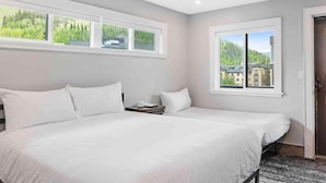 A bedroom with a large bed, two windows, and a view of a building and trees.
