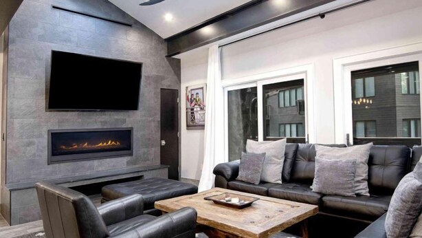 A modern living room with a fireplace, leather sofa, and a flat-screen TV mounted on the wall.