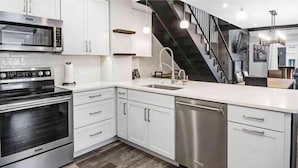 A modern kitchen with stainless steel appliances, white cabinetry, and a black staircase.