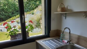 Une cuisine dotée d’un évier en acier inoxydable, d’une fenêtre donnant sur un jardin et d’une étagère sur laquelle se trouve un panier.