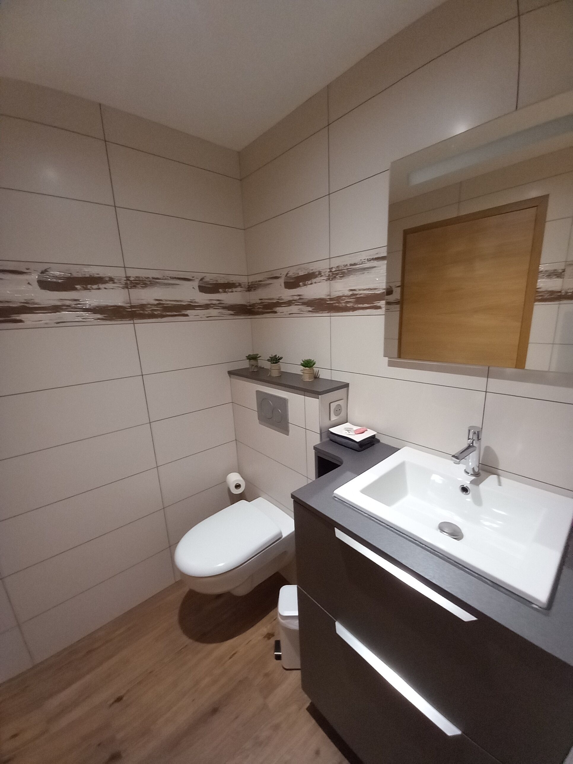 Une salle de bain moderne avec des toilettes blanches, un lavabo et un miroir au-dessus.