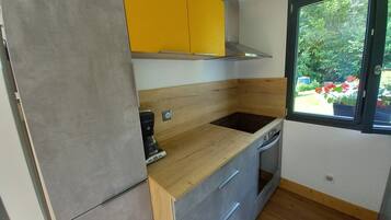 Een compacte keuken met een ingebouwde kookplaat, een koffiezetapparaat en een raam met uitzicht op groen.