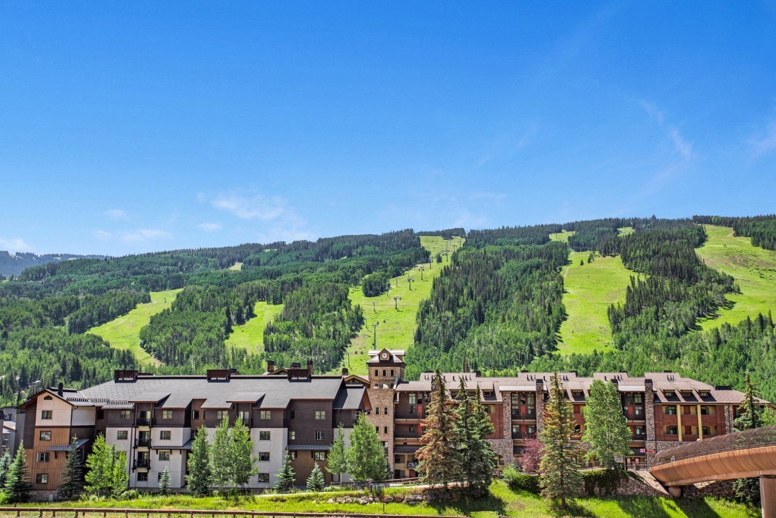 Un hotel con diversi edifici, una pista da sci sullo sfondo e un cielo azzurro limpido.