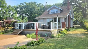 A two-story house with a covered porch, a fenced deck, and a brick chimney. - Riverfront Charmer with Character & Entertainment (McHenry)