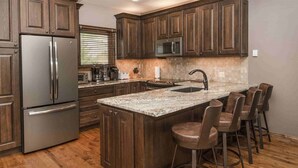 A kitchen with dark wooden cabinets, stainless steel appliances, a granite countertop, and bar stools.