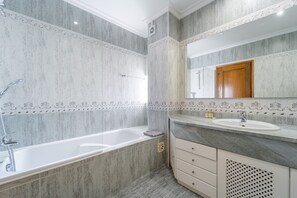 A modern bathroom with a freestanding bathtub, a vanity with a sink, and a large mirror. - Villa Lemos by HelloVacations (Albufeira)