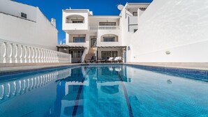 A swimming pool with clear blue water, surrounded by white buildings with balconies and a staircase leading to the upper floors. - Villa Lemos by HelloVacations (Albufeira)