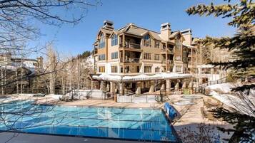Un hotel de varios pisos con un área de piscina, que incluye una piscina grande y un jacuzzi más pequeño.