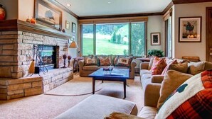 A cozy living room with a stone fireplace, a large window with a view of a green landscape, and comfortable seating.