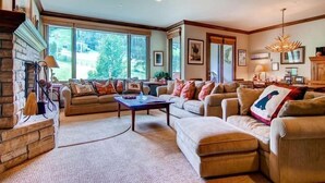 A spacious living room with a fireplace, large windows, and a chandelier.