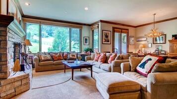 A spacious living room with a fireplace, large windows, and a chandelier.