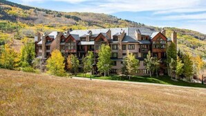 A multi-story hotel with a traditional architectural style, featuring a mix of stone and wood exteriors, set against a backdrop of autumnal trees and a hilly landscape.