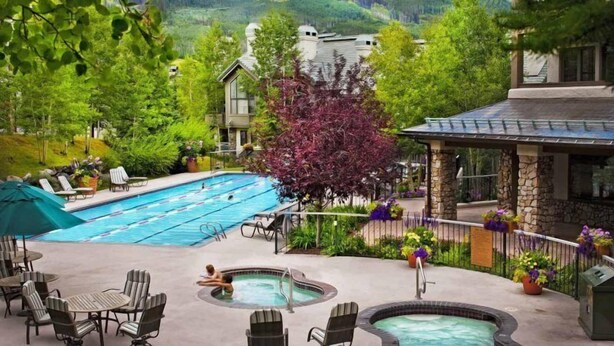 A pool area with a hot tub, lounge chairs, and a view of a mountain.