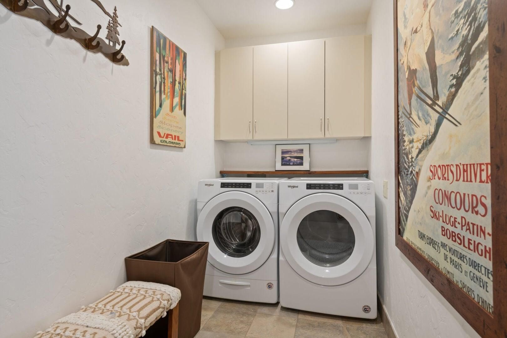 Un cuarto de lavado con dos lavadoras Whirlpool, un pequeño banco y un cartel en la pared.