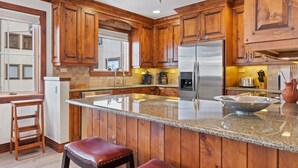 A kitchen with wooden cabinets, a stainless steel refrigerator, granite countertops, and a large island with stools. - Beaver Creek Centennial 2 Bedroom Residence (Avon)
