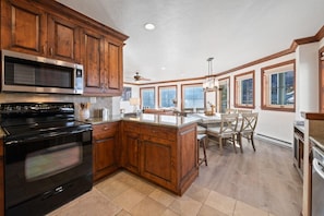 A kitchen with wooden cabinets, a black stove, and a dining area with a chandelier.