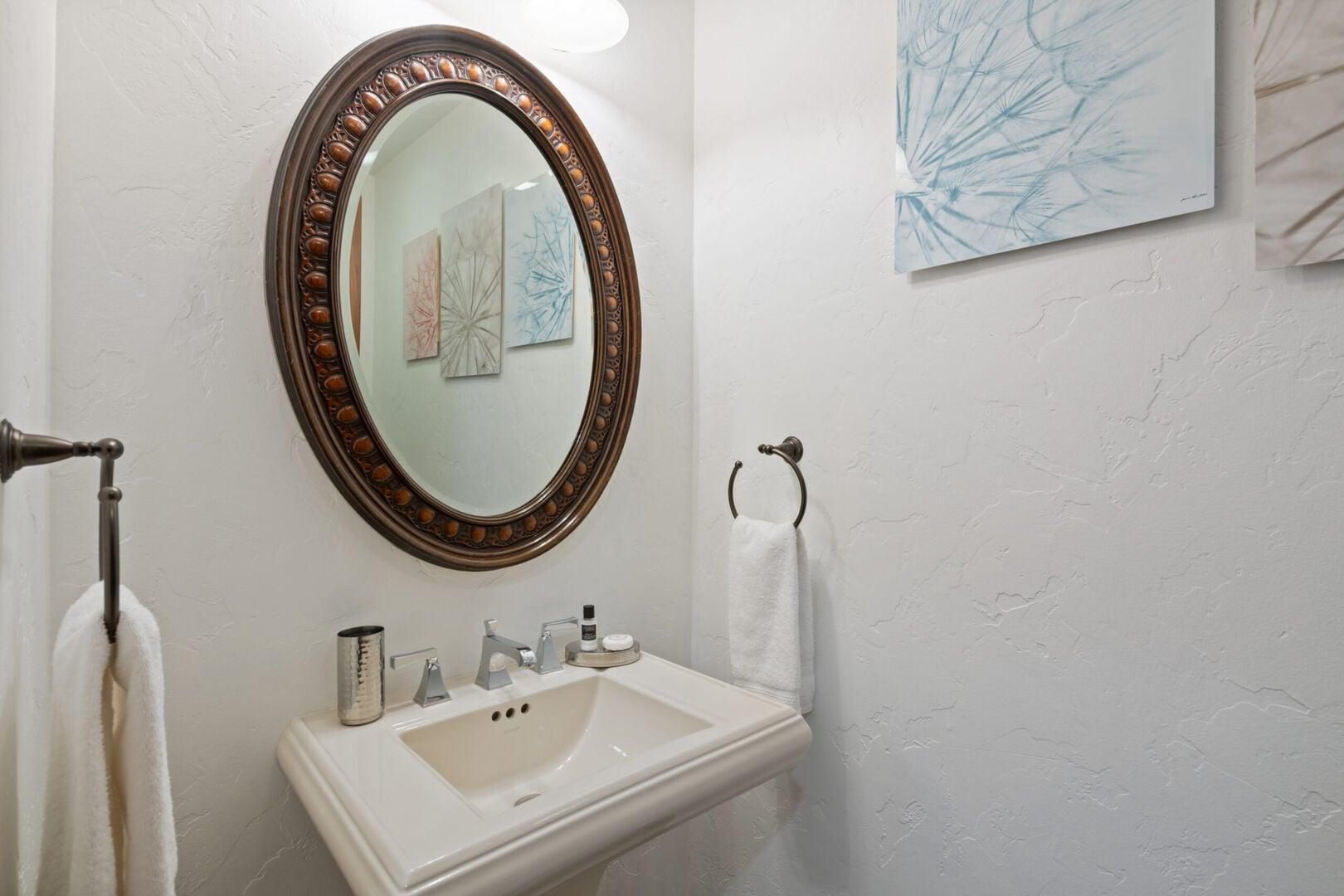 A bathroom with a white sink, a mirror with a decorative frame, and a towel rack.