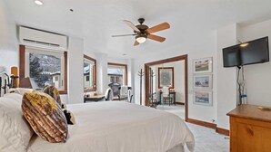 A bedroom with a large bed, a ceiling fan, a TV, and a view of the outside. - Beaver Creek Centennial 2 Bedroom Residence (Avon)