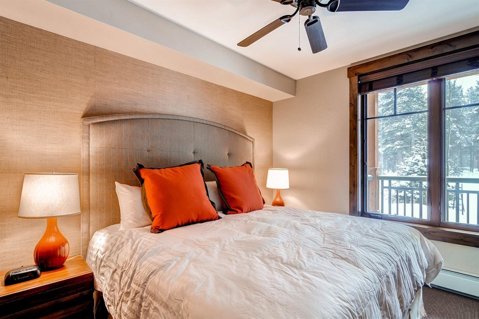 A hotel room with a large bed, two nightstands, a ceiling fan, and a window with a view of trees.