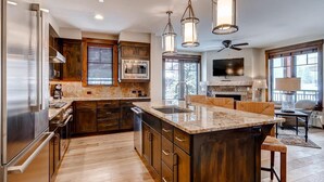 Una cocina moderna con armarios de madera, una isla grande, electrodomésticos de acero inoxidable e iluminación colgante.