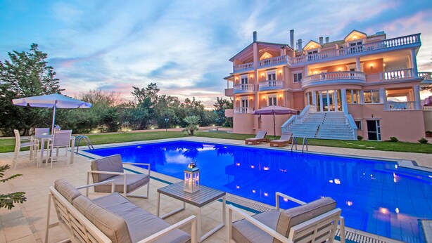 Une grande maison avec une piscine, du mobilier d’extérieur et un balcon bien éclairé.
